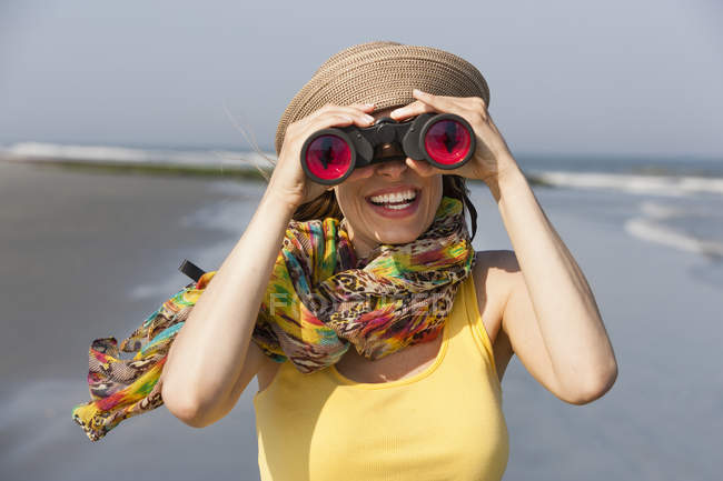 Woman in sunhat and scarf using binoculars on beach on New Jersey Shore, USA. — Stock Photo