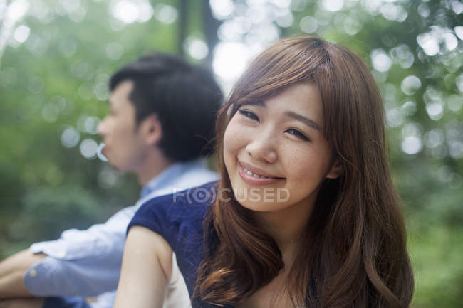 Junge Frau lächelt und blickt in die Kamera, während sie mit Mann im Park sitzt. — Stockfoto