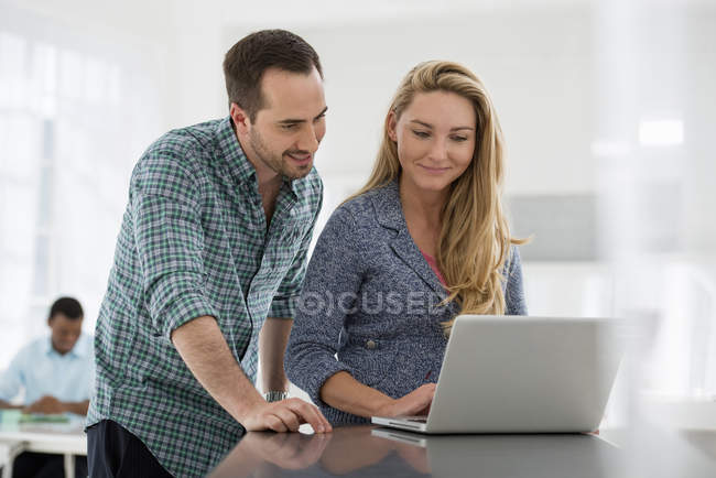 Un par de compañeros de trabajo mirando la pantalla de la computadora en la mesa de la oficina . - foto de stock