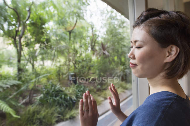Woman leaning on glass pane in city park with eyes closed. — Stock Photo