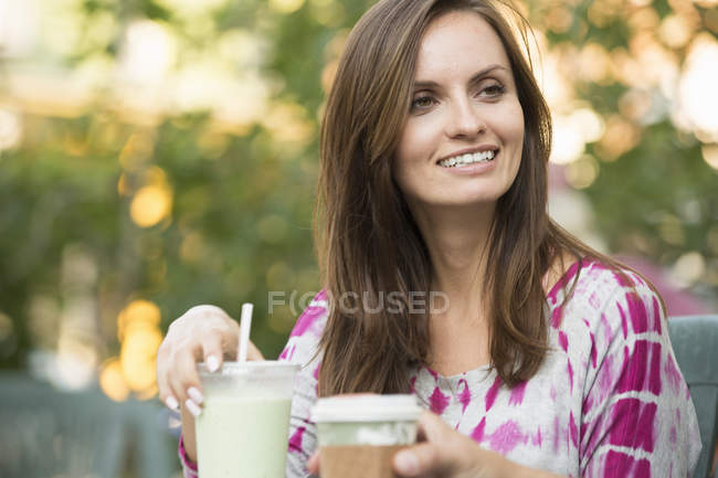 Frau sitzt mit Getränk in der Hand am Tisch im Freien. — Stockfoto