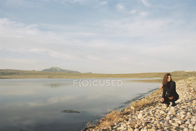 Mujer recogiendo guijarros en la orilla del lago de montaña . - foto de stock