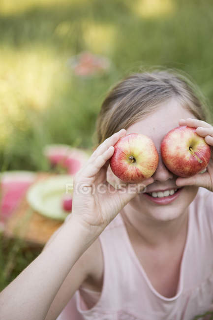 Niña de edad elemental sosteniendo manzanas delante de los ojos, retrato . - foto de stock