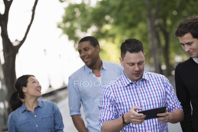 Cuatro personas caminando en la calle y hombre adulto medio usando tableta digital . - foto de stock