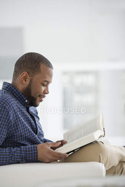 Mittlerer erwachsener Mann sitzt und liest Buch im hellen weißen Raum. — Stockfoto