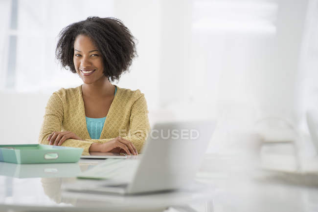 Femme avec les bras pliés assis au bureau avec ordinateur portable et dossier vert . — Photo de stock