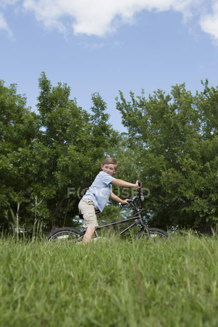 Menino da idade elementar andar de bicicleta através da grama no campo . — Fotografia de Stock