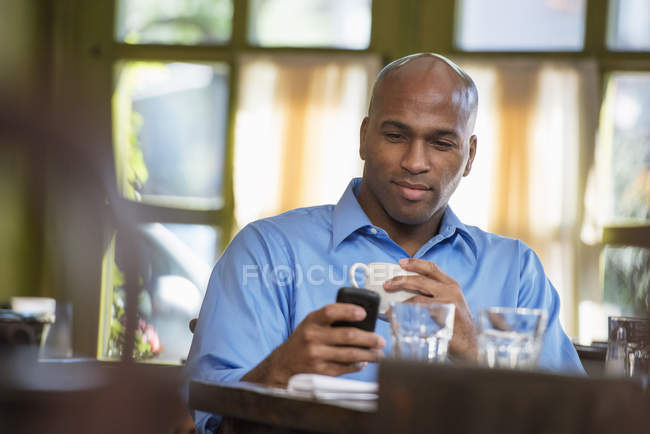 Businessman sitting in cafe with cup of coffee and checking phone. — Stock Photo