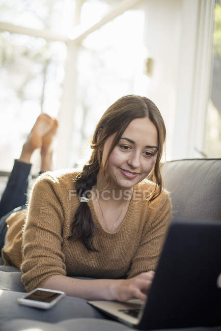 Femme allongée sur un canapé, souriante et regardant un ordinateur portable
. — Photo de stock