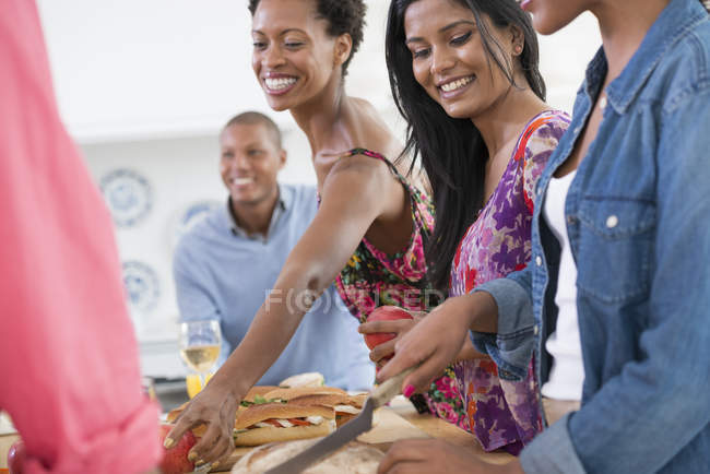 Groupe d'amis joyeux prenant de la nourriture à table buffet à la fête intérieure . — Photo de stock