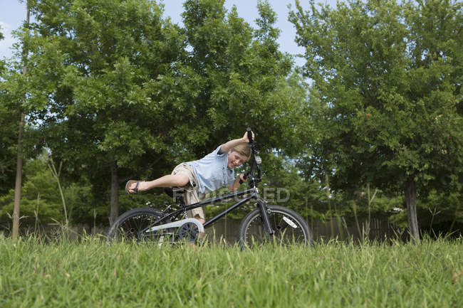 Menino da idade elementar caindo de bicicleta e superequilíbrio no campo gramado . — Fotografia de Stock