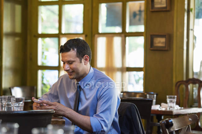 Mann sitzt allein am Stehtisch und checkt Smartphone. — Stockfoto