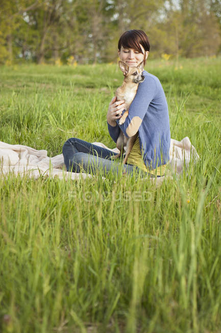 Young woman carrying chihuahua dog on blanket on grass field in park. — Stock Photo