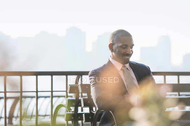 Homme d'affaires assis sur le banc de la ville, regardant vers le bas et souriant . — Photo de stock