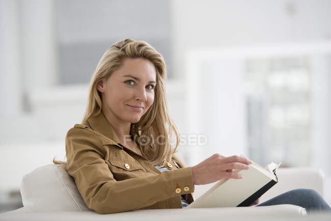Donna bionda seduta con libro nella luminosa stanza bianca . — Foto stock
