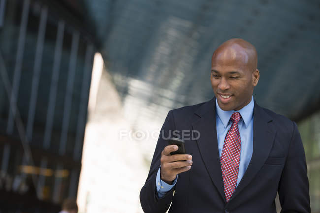 Geschäftsmann in Anzug und Krawatte lächelt und nutzt Smartphone in der Stadt. — Stockfoto