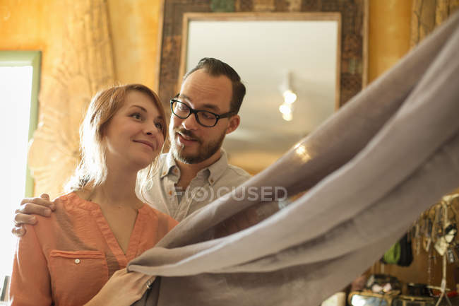 Homme et femme tenant un morceau de tissu de lin dans un magasin d'antiquités . — Photo de stock