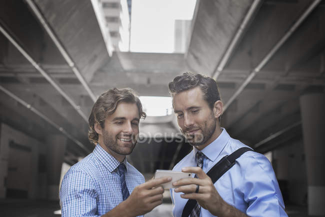 Two men in shirts and ties using smartphone with walkway and buildings in background. — Stock Photo
