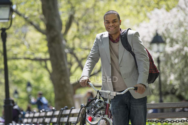 Mid adult man pushing bicycle in sunny park. — Stock Photo