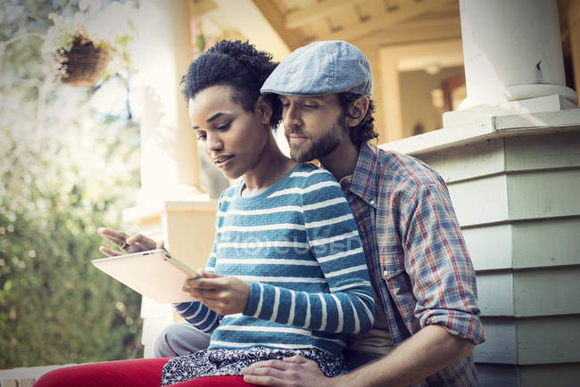 Paar sitzt auf Veranda Stufen und teilen digitales Tablet. — Stockfoto