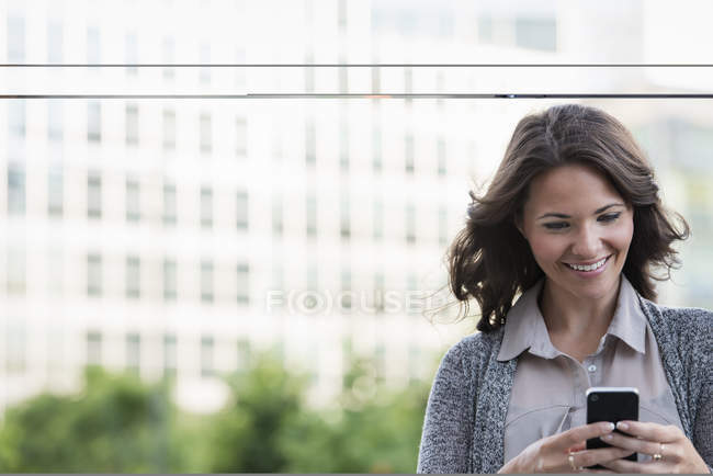 Businesswoman in grey cardigan using smartphone in city. — Stock Photo