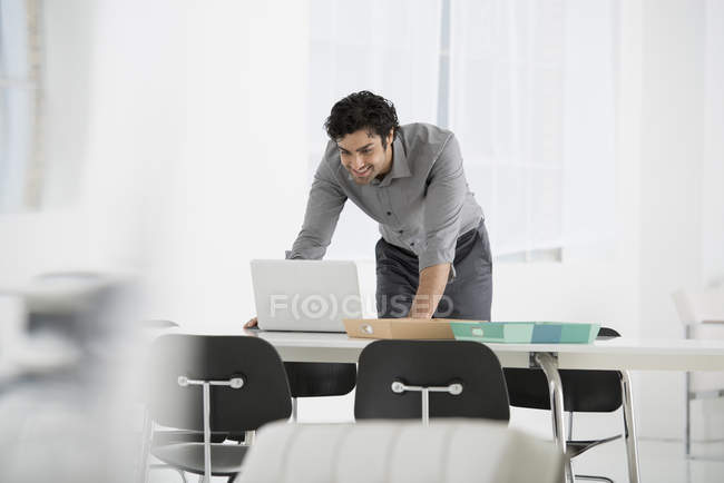 Молодий чоловік спирається вниз і використовує ноутбук в офісі . — стокове фото