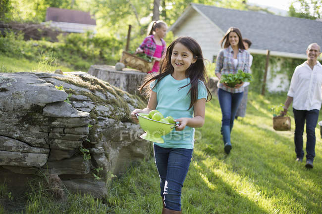 Familie trägt Körbe und Schalen mit Lebensmitteln über den Rasen im Bauerngarten. — Stockfoto