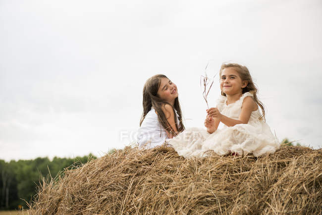 Two girls sitting on hay bale in countryside. — Stock Photo