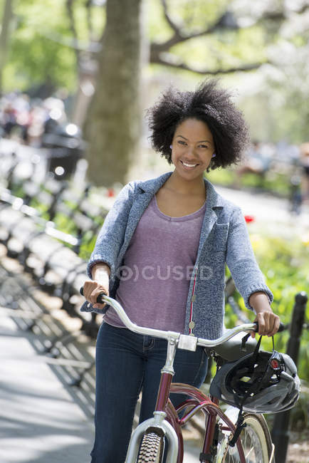Mitte erwachsene Frau mit Afro-Frisur in lässiger Kleidung schiebt Fahrrad im Park . — Stockfoto