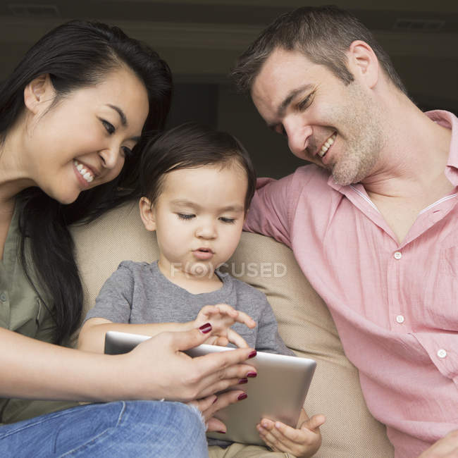 Los padres sentados en el sofá con su hijo y mirando la tableta digital . - foto de stock