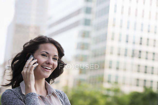 Young businesswoman in grey cardigan talking on phone in street. — Stock Photo