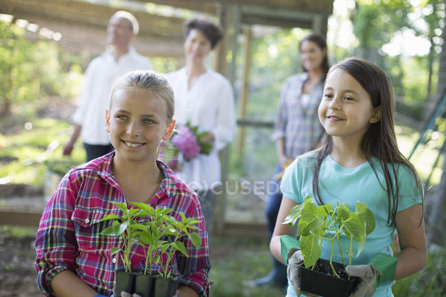 Ragazze che tengono giovani piante in vaso con coppia matura e giovane donna in background in fattoria . — Foto stock