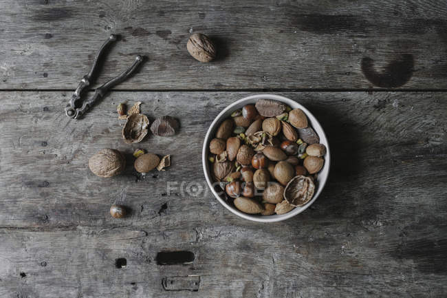 Bowl of mixed nuts, shells and nutcracker on table. — Stock Photo