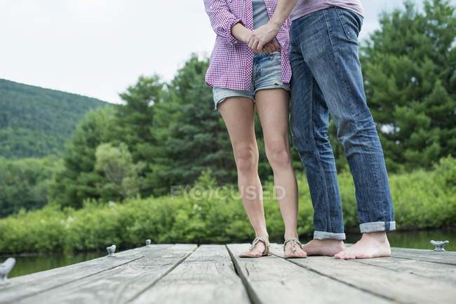 Пара тримає руки на дерев'яному джуті біля сільського озера . — стокове фото