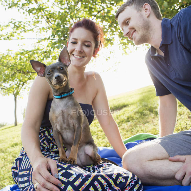 Metà coppia adulta a riposo con cane da compagnia chihuahua nel parco . — Foto stock