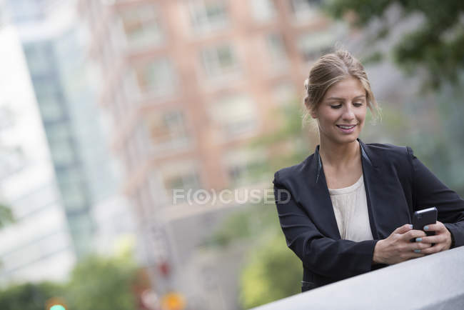 Молода бізнес-леді в чорній куртці за допомогою смартфона в місті . — стокове фото