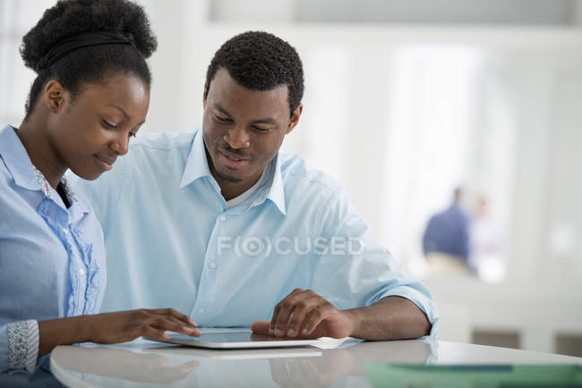 Hombre y mujer sentados uno al lado del otro y usando tableta digital en la oficina
. - foto de stock