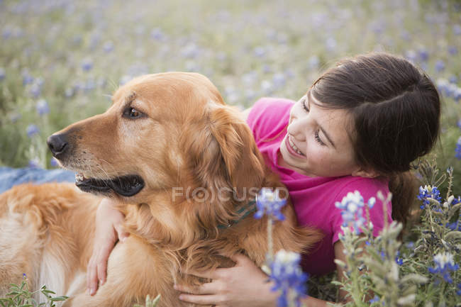 Mädchen im Grundalter umarmt Golden Retriever Haustier im Freien. — Stockfoto