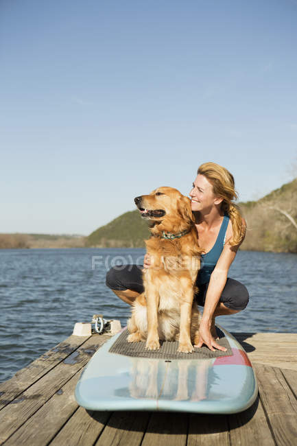 Mulher e cão retriever em paddleboard no molhe pelo lago . — Fotografia de Stock