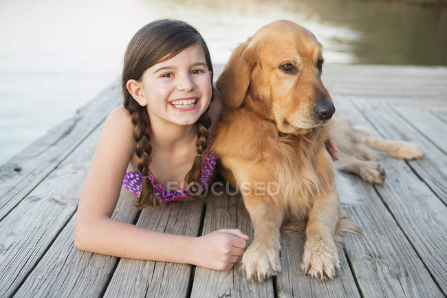 Pre-adolescent girl in swimwear with golden retriever dog lying on jetty. — Stock Photo