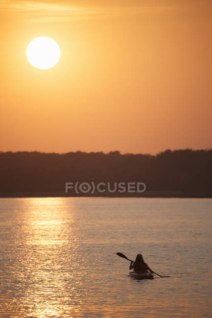 Kayakista hembra al atardecer en un lago tranquilo
. - foto de stock