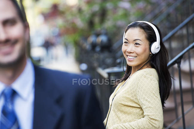 Woman wearing music headphones and man in business suit walking in foreground. — Stock Photo