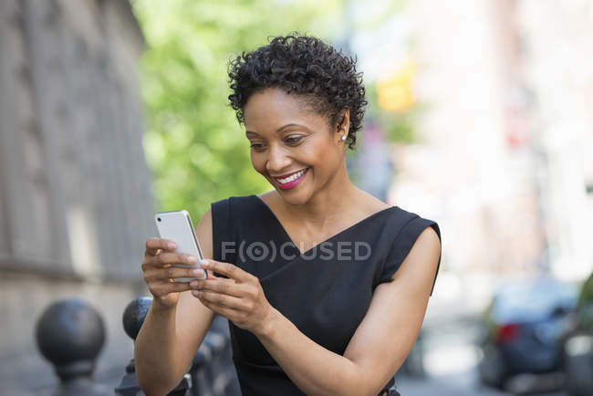 Mulher de vestido preto verificando telefone na rua da cidade . — Fotografia de Stock