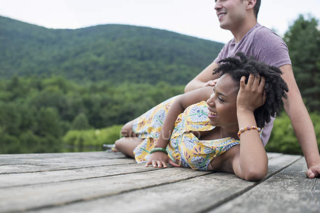 Casal jovem relaxante no molhe de madeira com vista para o lago da montanha . — Fotografia de Stock