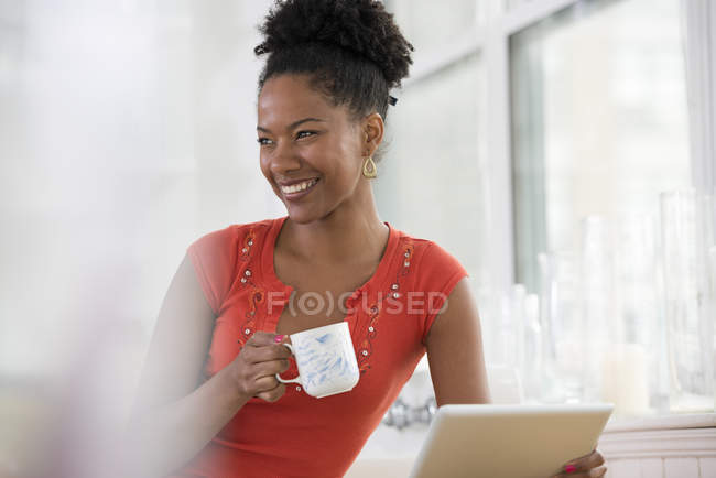 Metà donna adulta in possesso di tablet digitale e avere una tazza di caffè in cucina
. — Foto stock
