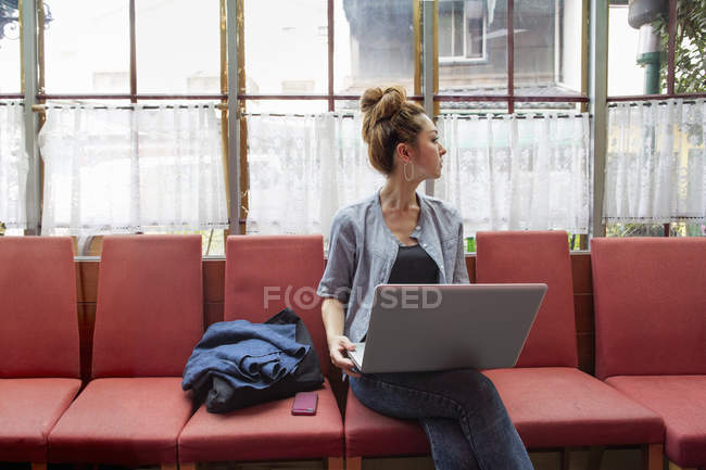 Mitte erwachsene Frau hält Laptop in der Hand und schaut drinnen weg. — Stockfoto