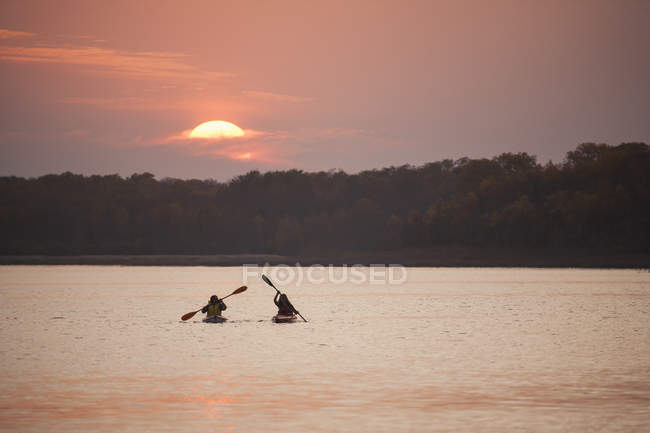 Two kayakers in boats at sunset on calm lake in Canada. — Stock Photo