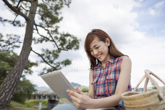 Junge Frau benutzt digitales Tablet und lächelt im Park. — Stockfoto