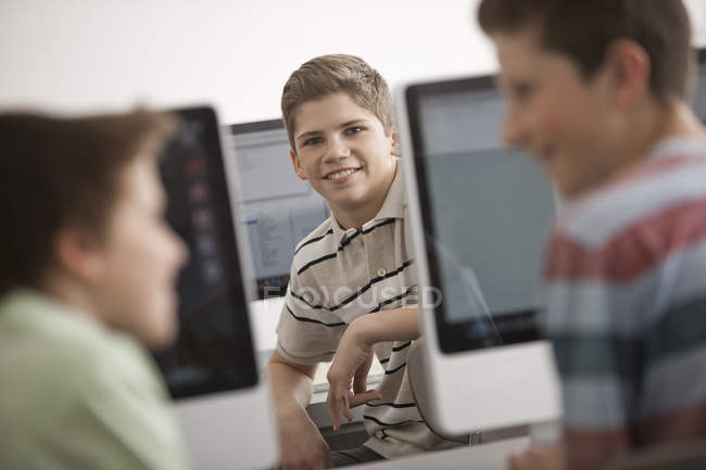 Niños pre-adolescentes sentados en laboratorio de computación con filas de monitores de computadora . - foto de stock