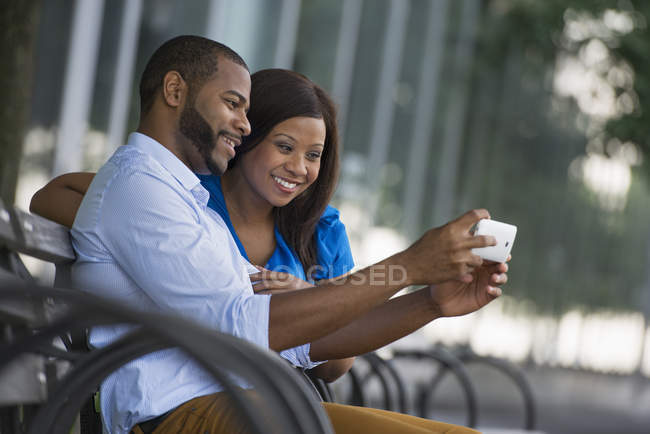 Couple sitting on bench and taking selfie in city. — Stock Photo